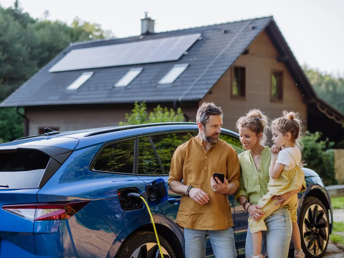 Junge Familie steht vor ihrem Einfamilienhaus mit Solaranlage auf dem Dach