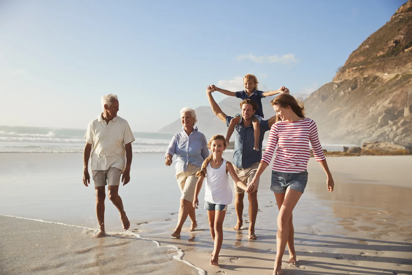 Großeltern, Eltern und Kinder spazieren gemeinsam barfuß am Strand