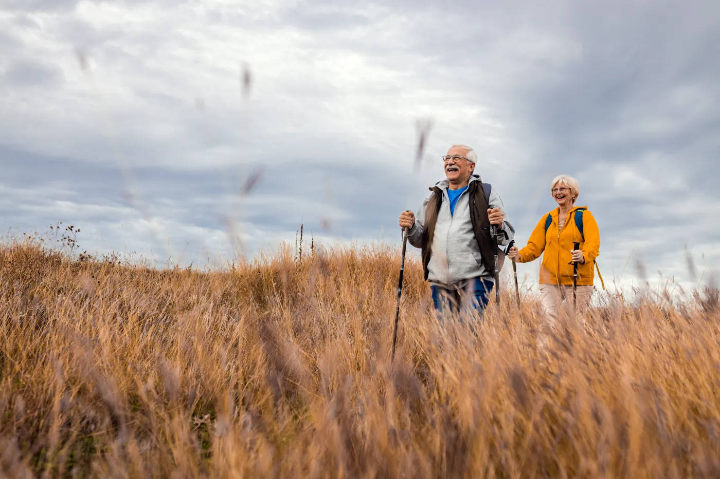 Älteres Paar wandert gut gelaunt mit Stöcken durch eine Graslandschaft